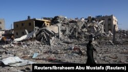 Një palestineze duke kaluar pranë një ndërtese të shkatërruar në Han Junis, në jug të Rripit të Gazës. 24 nëntor 2023.
