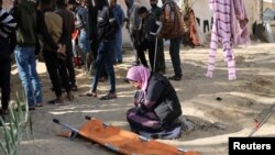 Жена, покрила лицето си с длани, клечи до празна медицинска носилка в двора на болницата "Насър" в Хан Юнис в Ивицата Газа, 22 януари 2024 г. Хората край нея погребват телата на свои близки в болничния двор, тъй като достъпът до гробището е ограничен поради израелска операция.