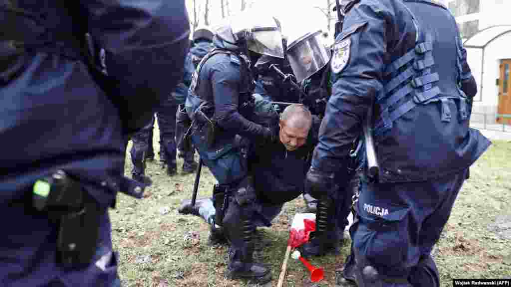 Policija drži muškarca tokom protesta ispred poljskog parlamenta. Dvadeset i tri osobe privedene su tokom nereda, u kojima je policija upotrijebila biber sprej, pendreke i šok bombe prema Reutersovom svedoku. Demonstranti su viđeni kako bacaju predmete, uključujući kamenje, na policiju.