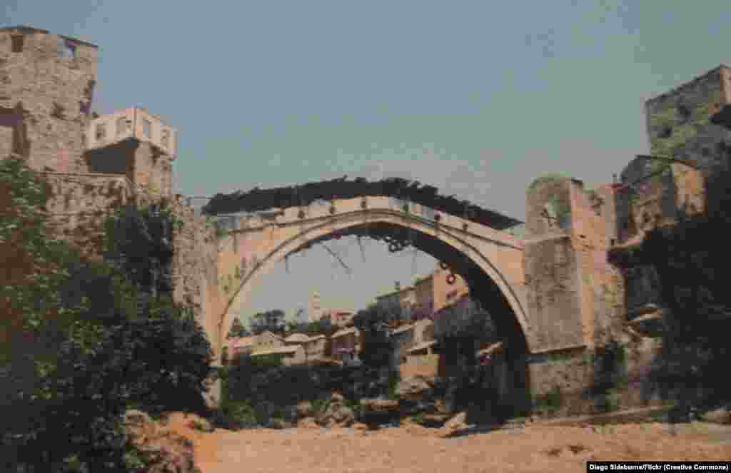 Тази снимка от август 1993 г. е една от последните на оригиналния мост в Мостар, Босна и Херцеговина, известен като Стари мост. Въпреки че е покрит с гуми и дървени дъски, за да бъде предпазен огъня от минохвъргачки и танкове, мостът пада в река Неретва след масирани удари на етнически хърватски сили през ноември 1993 г.