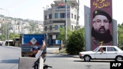 Čovek na mopedu pokazuje prstima znak za pobedu dok prolazi pored bilborda sa likom ubijenog glavnog komandanta Hezbolaha Fuada Šukra, dan posle njegove sahrane, Liban,2. avgusta 2024.