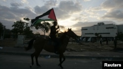 პალესტინელები დროშებენ აფრიალებენ ყოფილი ებრაული დასახლებების ნანგრევებზე. დაწვეს სინაგოგა. ღაზის სექტორის სამხრეთი ნაწილი. 2005 წლის 12 სექტემბერი.