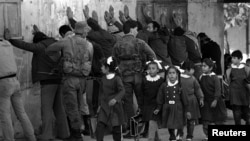 პალესტინელი სკოლის მოსწავლეები სახლში ბრუნდებიან გაკვეთილებიდან. ფონზე ისრაელის ჯარისკაცების არაბ მამაკაცებს ჩხრეკენ, მას შემდეგ რაც ებრაელი მამაკაცი მძიმედ დაჭრეს, 1986 წელი. 1987 წელს მასობრივი აჯანყება მოხდა, რომელიც ცნობილია როგორც „ინტიფადა“.