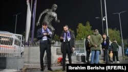 Dy tifozë izraelitë duke qëndruar pranë bustit të legjendës së futbollit shqiptar, Fadil Vokrri, pranë stadiumit i cili mban emrin e tij, para ndeshjes mes Kosovës dhe Izraelit në kualifikime për Euro 2024, 12 nëntor 2023.