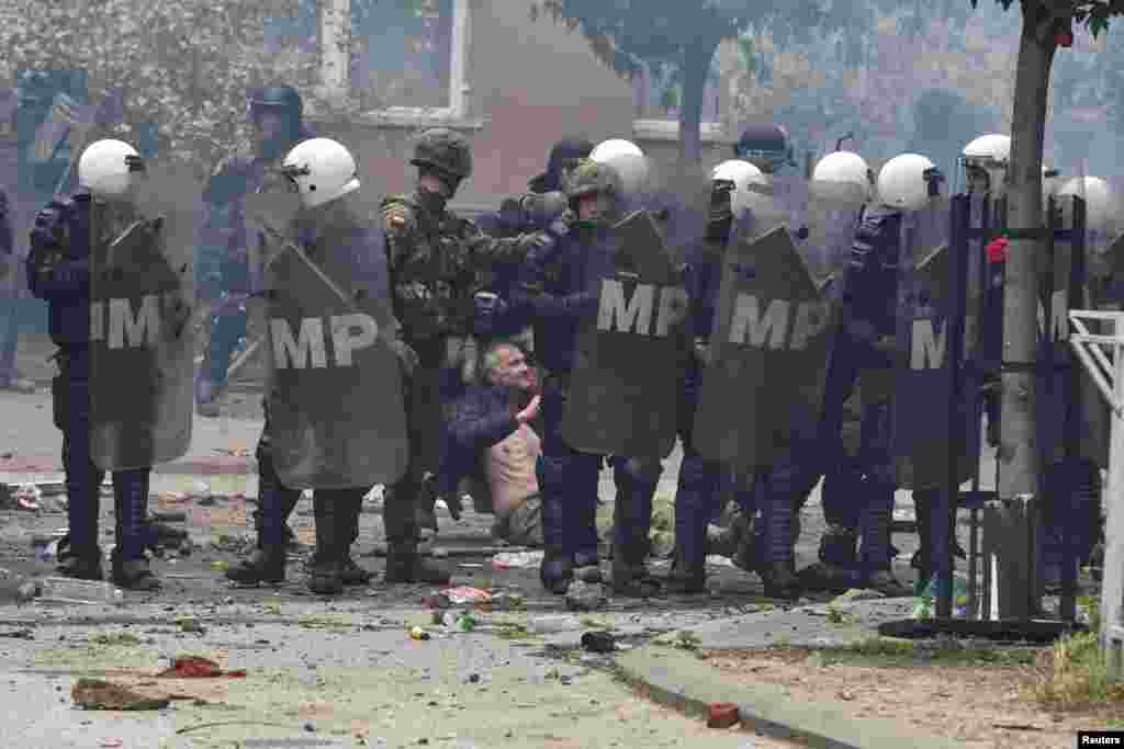 A KFOR-katonák feltartóztatnak egy helyi szerb tüntetőt az önkormányzati hivatalnál a koszovói Zvečanban 2023. május 29-én.&nbsp; A Szabad Európa újságírói a helyszínen arról számoltak be, hogy a tömegben sokan leültek, amikor a KFOR katonái elindultak, hogy kiszorítsák őket. Könnygázt észleltek, és sokkolóbombák robbantak, aminek egy része a tüntetőktől származhatott.&nbsp;A tüntetők köveket és palackokat is dobáltak a KFOR-csapatokra