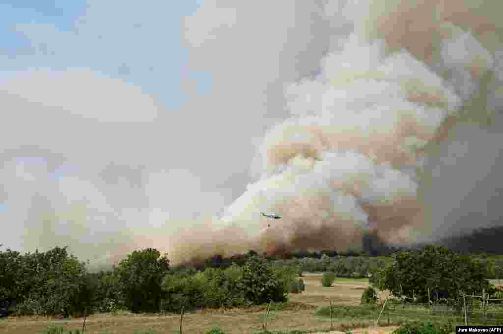 Një helikopter duke hedhur ujë mbi një re tymi të shkaktuar nga djegia e pyllit nga zjarri i egër, afër fshatit Novelo, Slloveni, më 22 korrik.