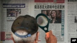 Muškarac koristi lupu da pročita novinski članak koji izvještava o posjeti predsjednice Predstavničkog doma američkog Kongresa Nensy Pelosy Aziji, na štandu u Pekingu, u nedjelju, 31. jula 2022. 