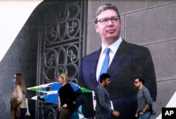 Emberek sétálnak egy választási óriásplakát mellett, amelyen Aleksandar Vučić jelenlegi szerb elnök és a Szerb Haladó Párt vezetője látható. Vučić kiáll Ukrajna területi integritása mellett, miközben nem hajlandó büntetni Moszkvát. Belgrád, 2022. március 28.