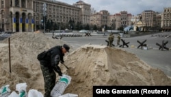 A man fills sandbags in the center of Kyiv on March 7 as volunteers from the Territorial Defense Forces patrol in the background.