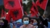 A woman looks on as people wave Albanian flags during a Socialist Party election rally in Tirana, Albania April 22, 2021.