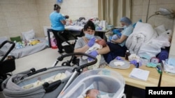 Оксана Мартиненко храни едно от 21 бебета на сурогатни майки в импровизираната клиника в подземие в Киев