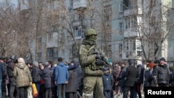 Ruski vojnik pored lokalnih stanovnika koji čekaju u redu za humanitarnu pomoć u opkoljenom Mariupolju.
