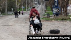 A woman pulls a wheelchair while transporting an injured man on a street in the southern port city of Mariupol on April 18.