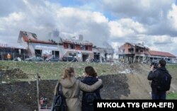 People look as Ukrainian rescuers put out a fire at an auto service center after Russian shelling in the western city of Lviv on April 18. According to authorities, seven civilians were killed.