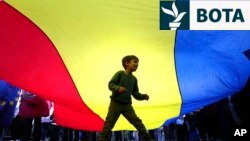 Një fëmijë luan poshtë një flamuri gjigant të Rumanisë, gjatë një eventi elektoral në mbështetje të kandidatit për president, Nicusor Dan, në Bukuresht më 11 maj.
