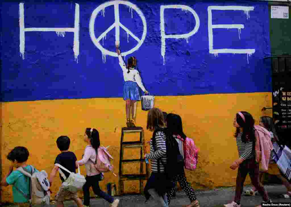 Ученици во Барселона, Шпанија, поминуваат покрај муралот на уметникот TVBOY на 9 мај. Мировниот симбол на сликата првично беше дизајниран за британското движење за нуклеарно разоружување во 1958 година.