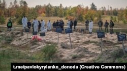 Polițiști și experți criminaliști examinează o groapă comună descoperită în regiunea Donețk din Ucraina în octombrie 2022.