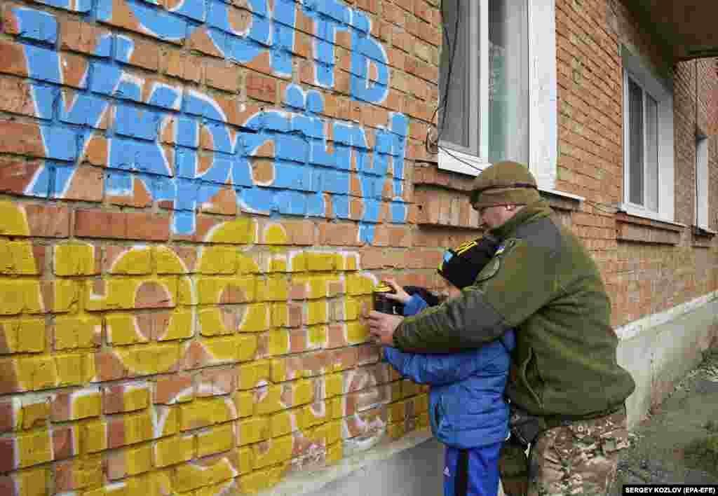 Un bărbat și un băiat pictează cu sprayul un mesaj de mândrie națională: &quot;Iubim Ucraina. Îl iubim pe Șevcenko&quot;.