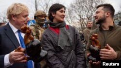 Președintele Ucrainei, Volodymyr Zelenskiy, și premierul britanic, Boris Johnson, țin în mână cocoși din ceramică identici cu cei găsiți printre resturile unei case distruse în timpul invaziei Rusiei, înBorodianka, 9 aprilie 2022