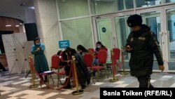 Сотрудница полиции на фоне наблюдателей, сидящих за ограждениями на избирательном участке, где голосовал президент Казахстана. Астана. 20 ноября 2022 года