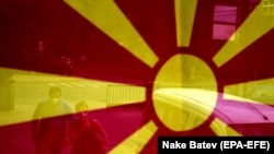 Glasaši na putu ka biračkom mestu u Skoplju, viđeni kroz makedonsku zastavu, u vreme parlamentarnih izbora u S. Makedoniji u julu 2020. godine