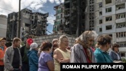 Helyi lakosok humanitárius segélyre várnak egy lebombázott lakóépületnél Borogyankában, Kijev közelében 2022. június 21-én