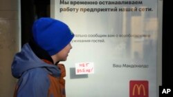 Un client trece pe lângă un mic afiș pe care scrie „Nu războiului!" lipit pe fereastra unui McDonald's unde se anunță închiderea restaurantului din Sankt Petersburg, Rusia, marți, 15 martie 2022