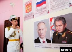 Oficir ruske mornarice se priprema za ceremoniju za diplomce na Pomorskoj akademiji, pored portreta ruskog predsjednika Vladimira Putina i ministra odbrane Sergeja Šojgua, Kaljiningrad, Rusija, 19. juni 2021.