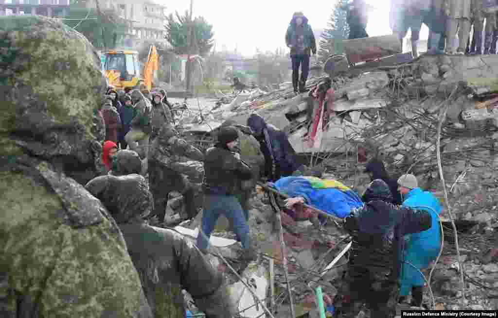 Руски војници и сириски цивили за време на напорите за пребарување и спасување во сирискиот регион Латакија на слика објавена на 7 февруари. Сирија е заглавена во децениска граѓанска војна, а областите погодени од земјотресот во Сирија, наводно, се поделени меѓу владата - контролирани и поддржани од бунтовниците области на земјата.