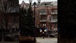 Un locuitor din Herson flutură steaguri ucrainene în fața unei coloane de tancuri parcate n centrul orașului.