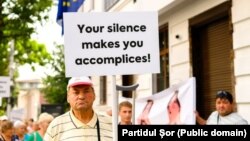 Un bărbat cu o pancartă pe care scrie „Tăcerea voastră vă face complici”, la protestul organizat de Partidul Șor și PCRM, în fața sediului Delegației UE, Chișinău, 26 august 2022