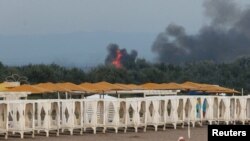 De pe o plajă la Marea Neagră, oamenii privesc fumul și flăcările după exploziile de la o bază aeriană militară rusă din Novofedorivka, Crimeea, în august 2022