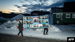 Ljudi nose veliki poster Demokrata sa slikom lidera te stranke Jens-Frederikom Nilsen pored glasačkog mesta tokom izbora na Grenlandu, 11. mart 2025.