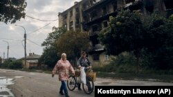 Doi localnici trec pe lângă o clădire distrusă de război în centrul orașului Izium din regiunea ucraineană Harkov, recent eliberată. 13 septembrie 2022.