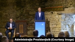 Klaus Iohannis vorbește în timp ce prietenul său, Michael Schmidt, îl ascultă așezat pe scaun.