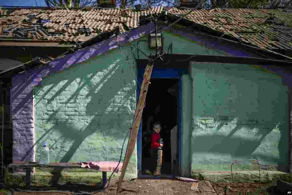 Egy kisfiú áll játékával a kezében otthonuk ajtajában, Pokrovszkban, Ukrajna keleti részén. A ház a harcokban megsérült