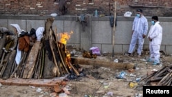 Dva člana porodice stoje pored lomače koja odnosi tjelo njihovog rođaka preiminulog od posledica infekcije korona virusom u glavnom gradu Indije Nju Delhiju. 22. spril 2021. 