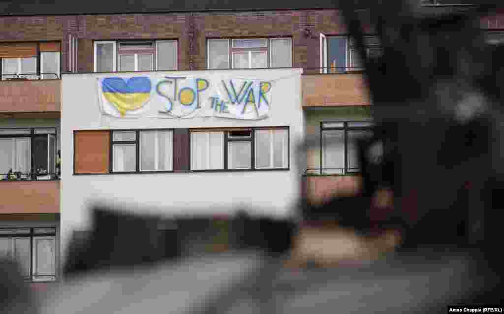 Antiratni znak visi sa stambene zgrade koja gleda na ruska vozila u Pragu. Ilja Kučinski, ukrajinski dobrovoljac i pripadnik teritorijalnih odbrambenih snaga, koji je pripremao izložbu za otvaranje 11. jula, rekao je za RSE da je cilj &bdquo;da podseti ljude da rat nije tako daleko koliko oni misle&quot;. &quot;Jer ako ne izdržimo, Češka je jedna od sledećih. I budite sigurni, [Rusija] se neće zaustaviti.&quot;