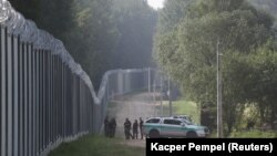 Гранични службеници покрај ѕидот подигнат за да го спречат преминувањето на мигрантите на полско-белоруската граница во услови на мигрантска криза во близина на Кузница, Полска, 30 јуни 2022 година