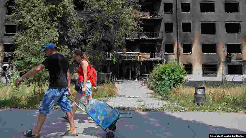 Lokalni stanovnici nose flaše vode pored uništenih stambenih zgrada. &nbsp;