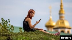 O femeie se uită în telefonul mobil. Pe fundal - biserici din orașul Suzdal, regiunea Vladimir, Rusia.