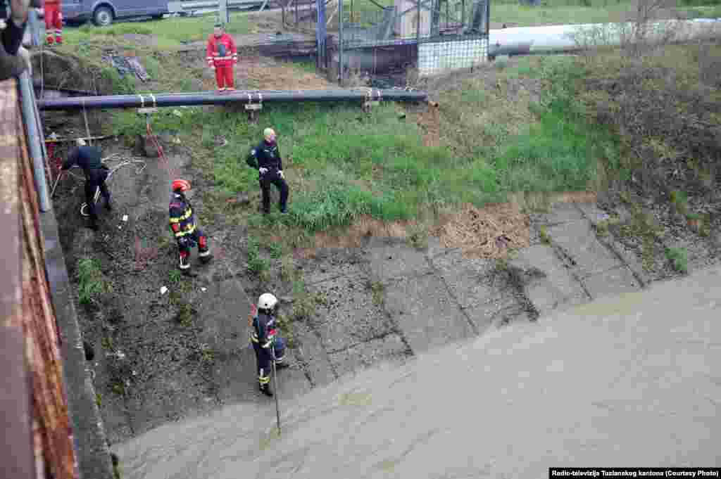 U Tuzli i okolini traje potraga za dvije osobe koje su nestale u nabujaloj rijeci.Riječ je o policajcu i jednoj osobi koja je bježala od policije u prijepodnevnim satima, 27. marta.Foto: Vatrogasci pored korita rijeke u potrazi za dvije osobe, Tuzla, Bosna i Hercegovina.