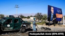 An Afghan security official stands beside a billboard featuring vice-presidential candidate Amrullah Saleh as he inspects the scene of a suicide bombing that targeted a campaign rally of the incumbent president.