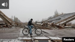 Локален човек вози велосипед во близина на уништениот мост во градот Покровск, во близина на линијата на фронтот во регионот Доњецк, Украина, 19 декември 2024 година.