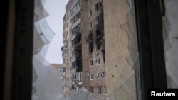 Низ скршен процорец се гледа зграда оштетена од руски воен напад во градот Вухледар, Украина, на 18 февруари 2023 година.