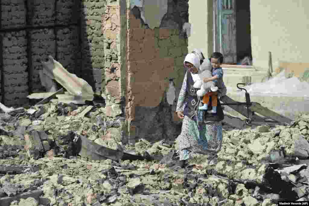 Кыргызка с маленьким ребенком пробирается через руины своего дома в селе Максат недалеко от границы с Таджикистаном, 4 мая 2021 года. Соседние страны, Кыргызстан и Таджикистан, согласились отвести войска от своих границ после ожесточенных боев, в результате которых погибло около 40 человек и было ранено 175. Государства заявляют права на территорию вокруг источника воды. Спор начался несколько десятилетий назад, когда обе республики были в составе Советского Союза