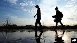 Dy njerëz duke ecur mbi një pellg uji në një rrugë në Afrikën e Jugut, më 26 maj 2023.