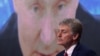 Dmitrij Peskov sjedi ispred ekrana na kojem se prikazan ruski predsjednik Vladimir Putin.