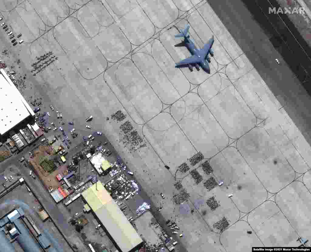 Gomile ljudi čekaju na asfaltu međunarodnog aerodroma Hamid Karzai u Kabulu dok ispred njih stoji transportni avion C-17 spreman za poletanje, 23. avgust 2021.