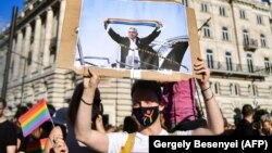 Протестиращ в Будапеща държи снимка, изобразяваща Виктор Орбан, който вдига шал с цветовете на дъгата